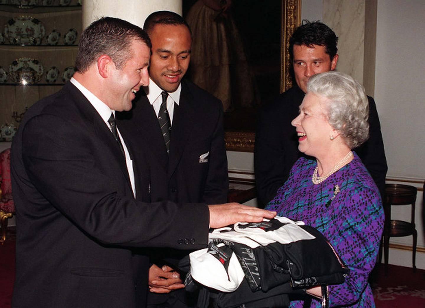 Queen Elizabeth II accepts autographed rugby jerys from All Blacks captain Sean Fitzpatrick (L), ably assisted by Jonah Lomu (centre) and Zinzan Brook
